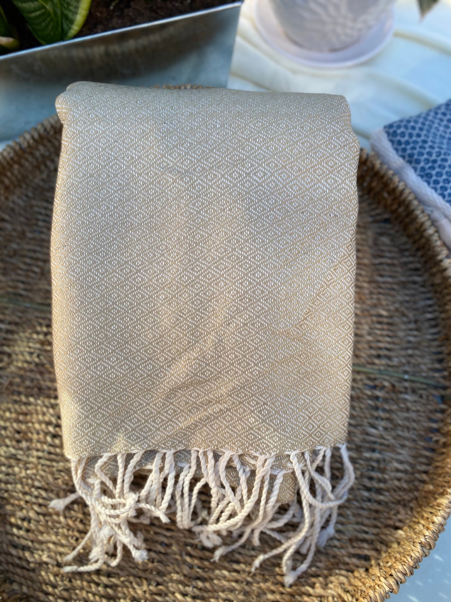 Light ecru coloured, diamond patterned, handwoven scarf lays in a basket on a table.