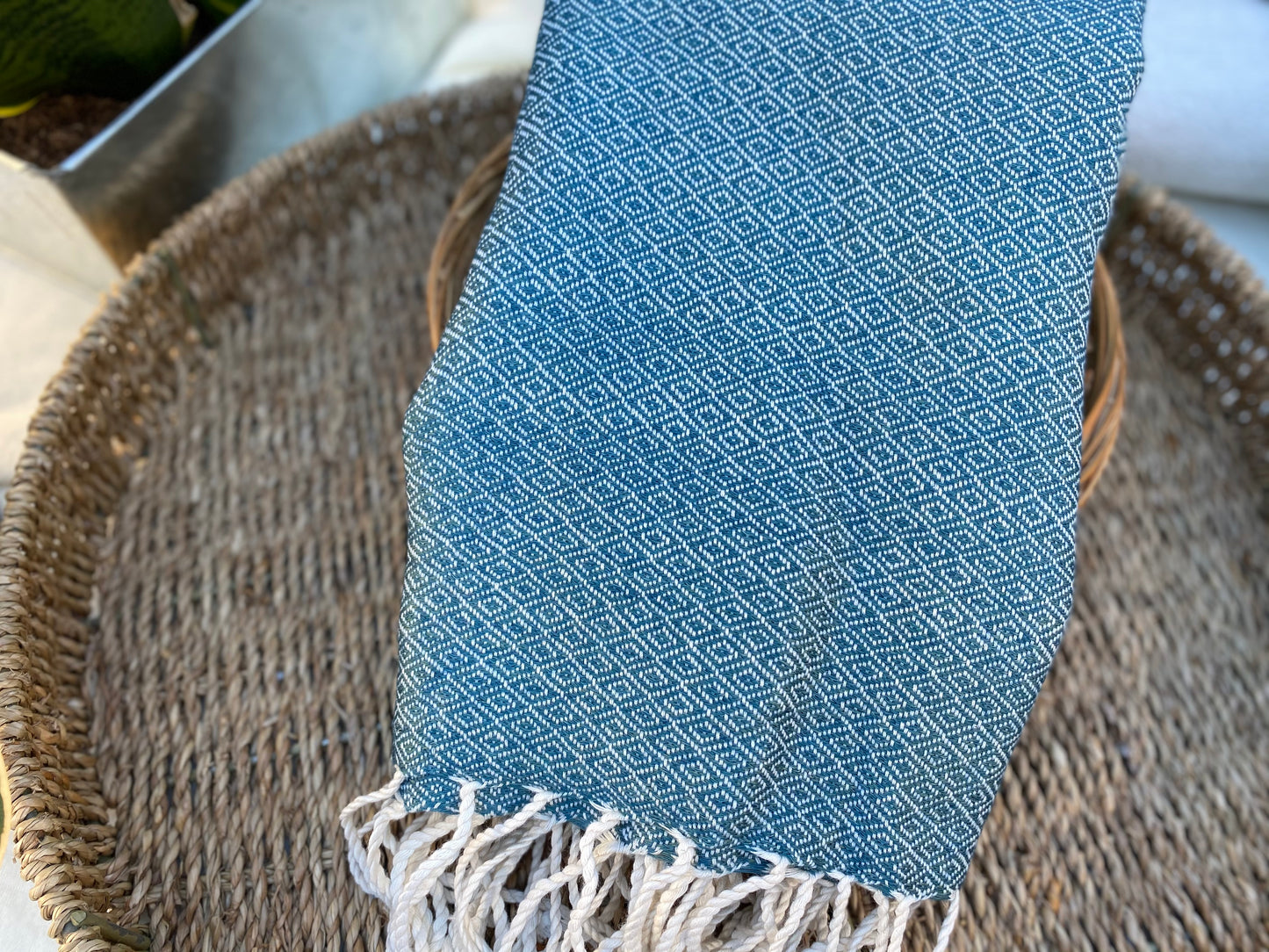 Dark blue coloured, diamond patterned, handwoven scarf lays in a basket on a table.