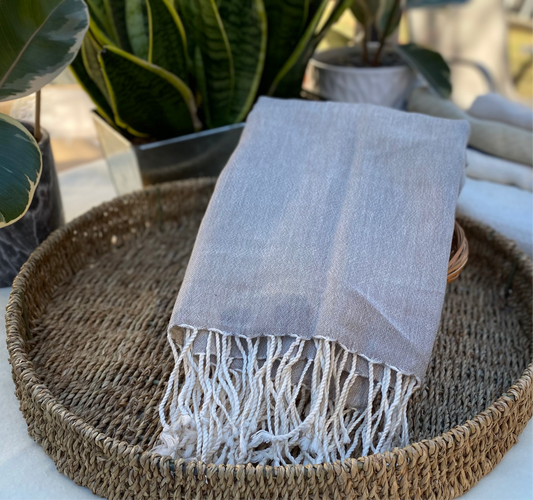 An ecru coloured scarf with off-white tassels lays on a flat basket.