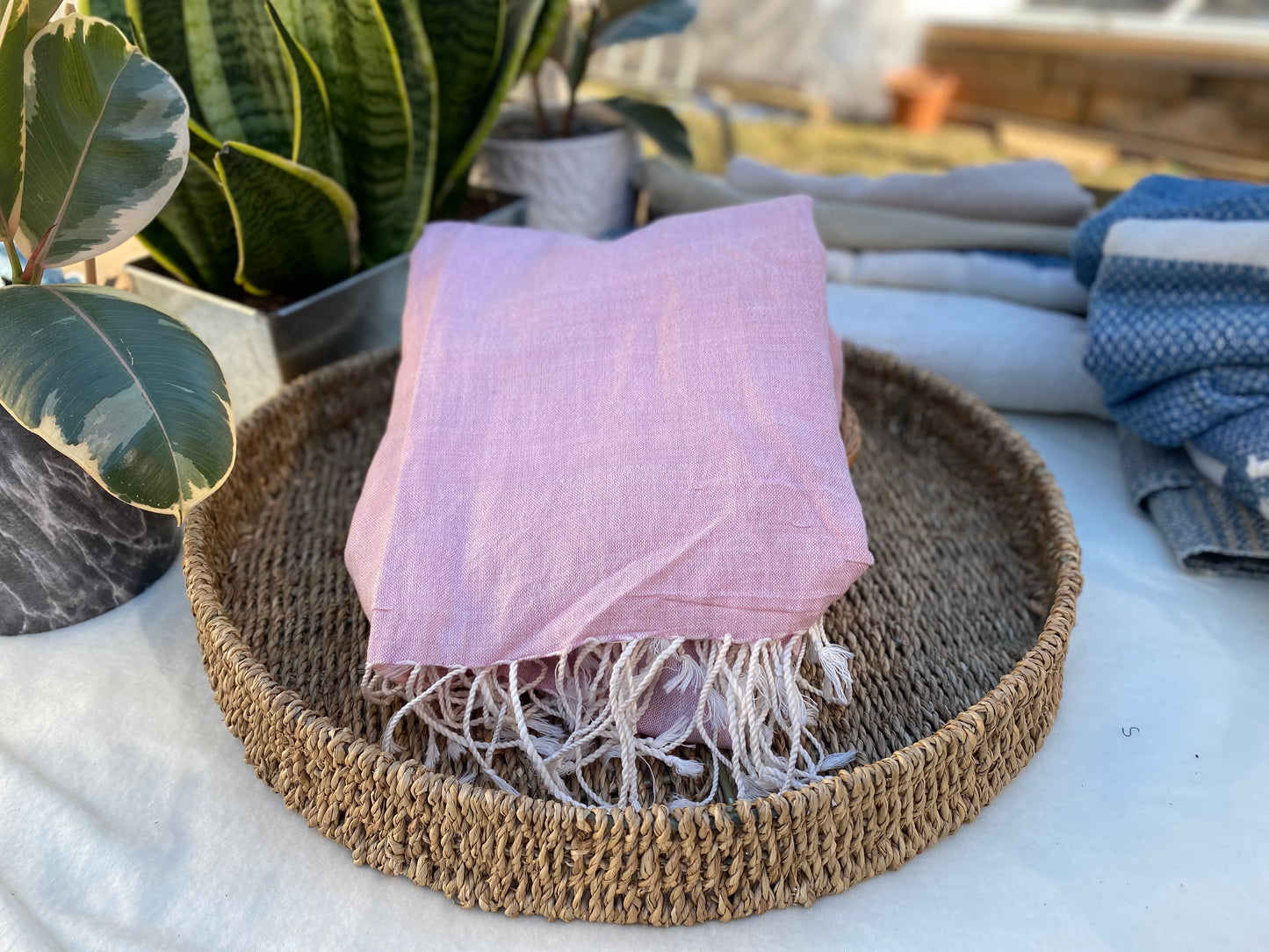 A light pink coloured scarf with off-white tassels lays on a flat basket.