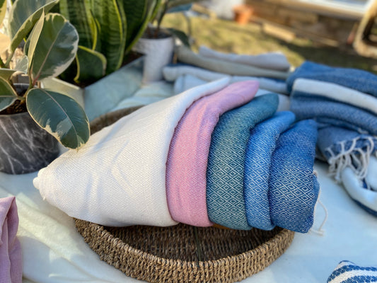 Five differently coloured, diamond patterned, handwoven scarves lay in a basket on a table.