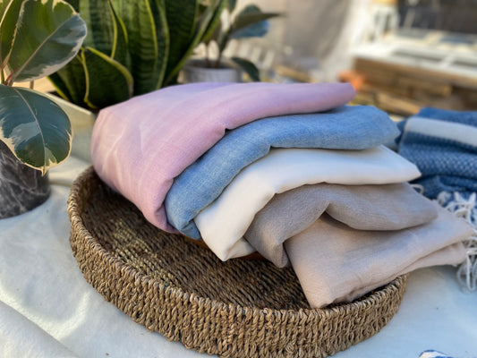 Five differently coloured scarves lay folded over in a basket on a table.