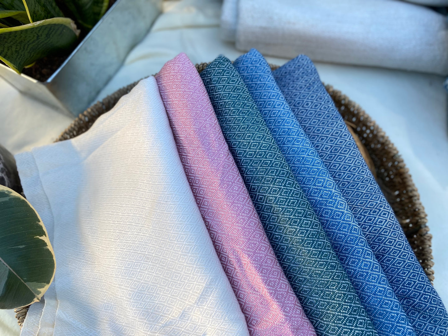 Several colours of diamond patterned, handwoven scarves lay in a basket on a table.