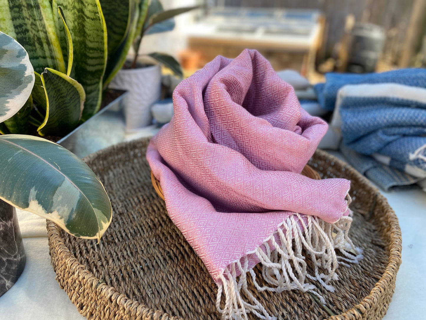 Light pink, diamond patterned, handwoven scarf lays in a basket on a table.