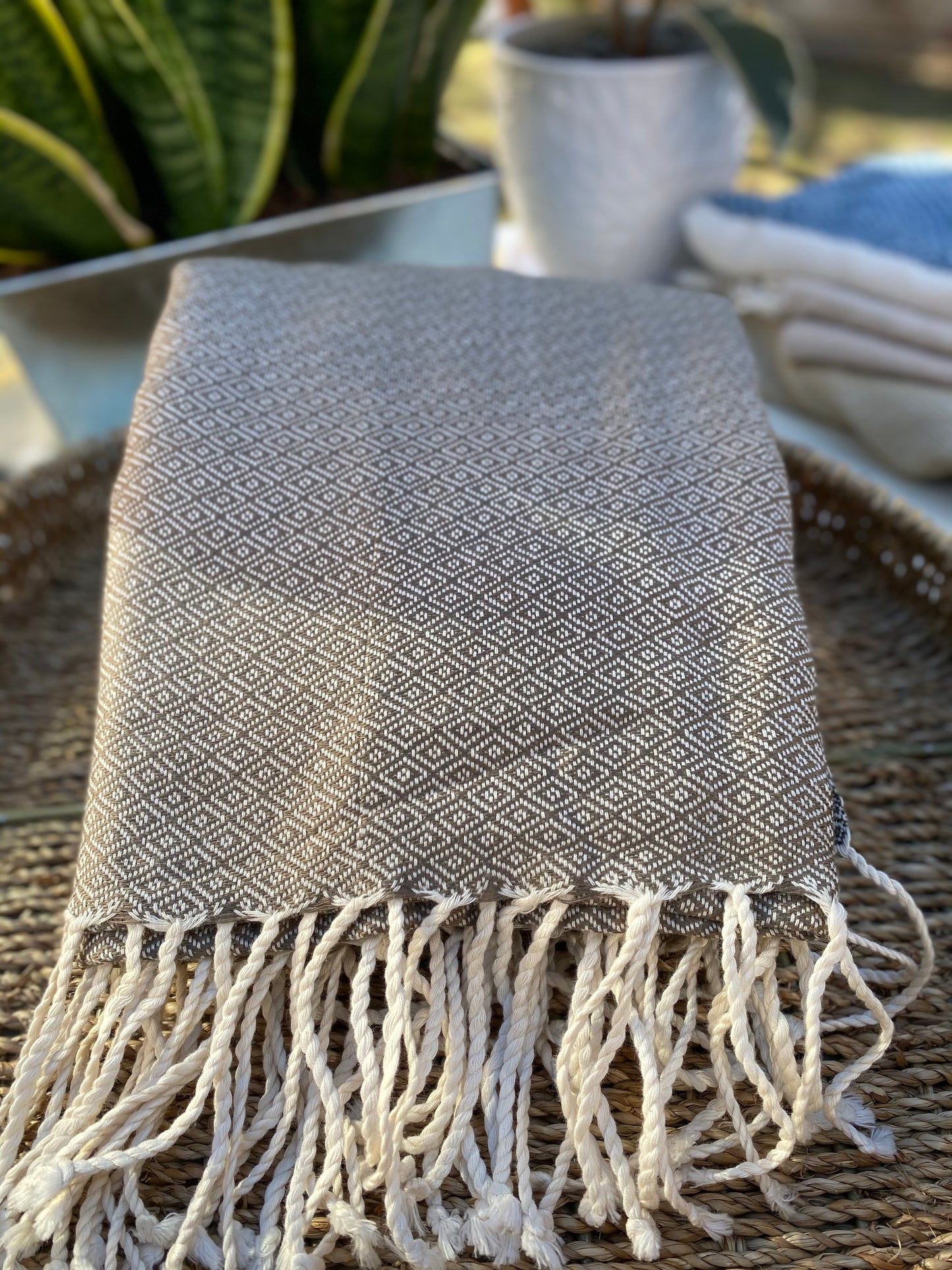 Dark ecru coloured, diamond patterned, handwoven scarf lays in a basket on a table.