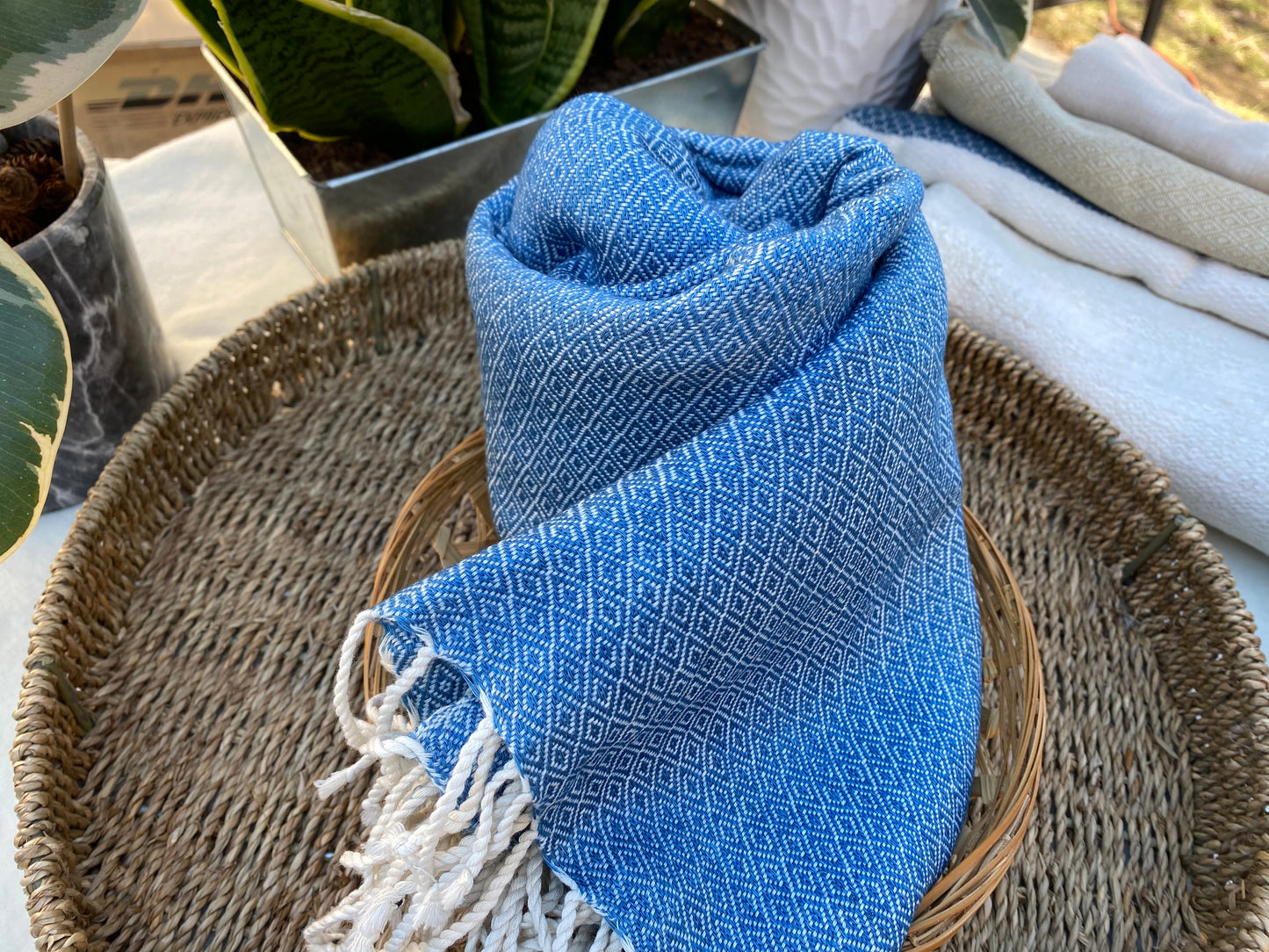 Dark blue coloured, diamond patterned, handwoven scarf lays in a basket on a table.