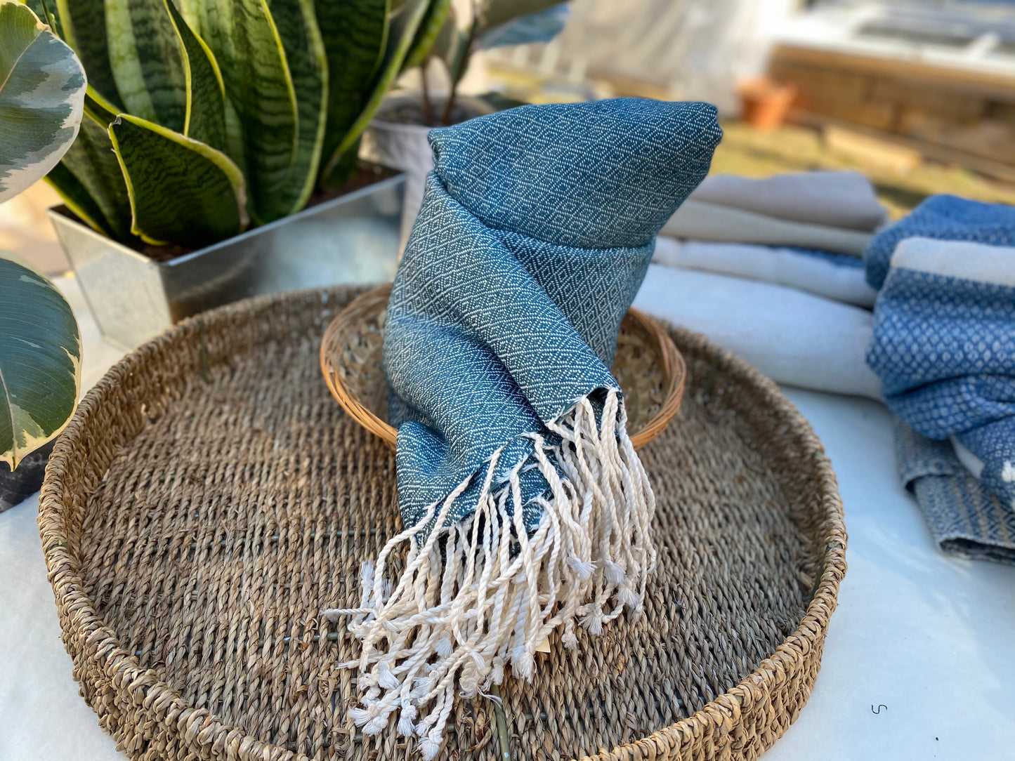 Dark teal coloured, diamond patterned, handwoven scarf lays in a basket on a table.